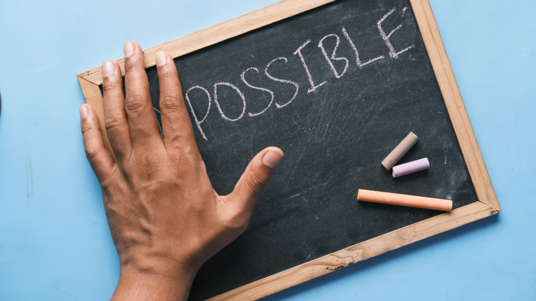 a chalkboard with the left hand covering the beginning letters of a word. The visible word is "possible."