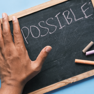 a chalkboard with the left hand covering the beginning letters of a word. The visible word is "possible."