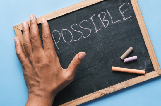 a chalkboard with the left hand covering the beginning letters of a word. The visible word is "possible."